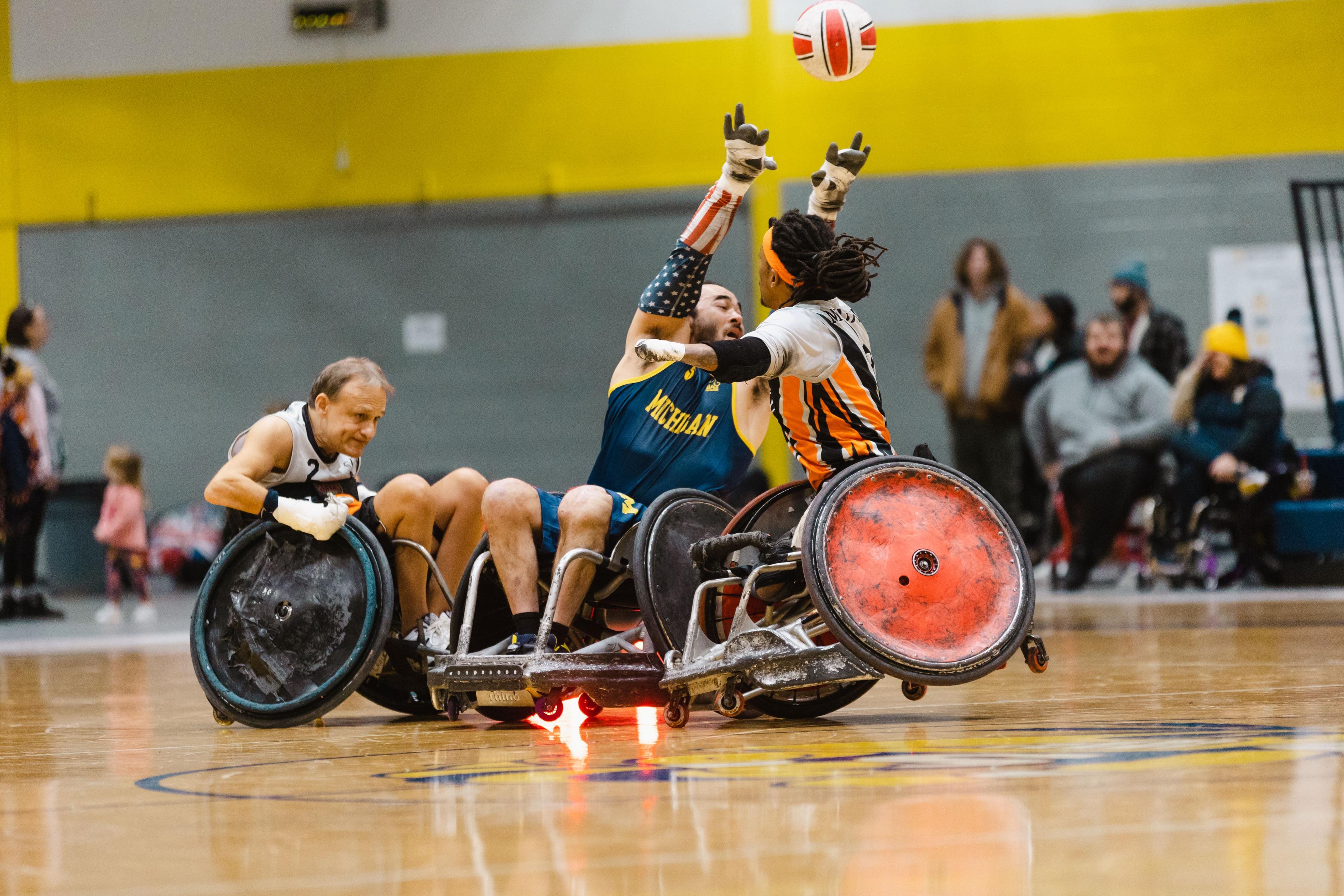 A wheelchair rugby athlete getting hit by another player while throwing the ball
