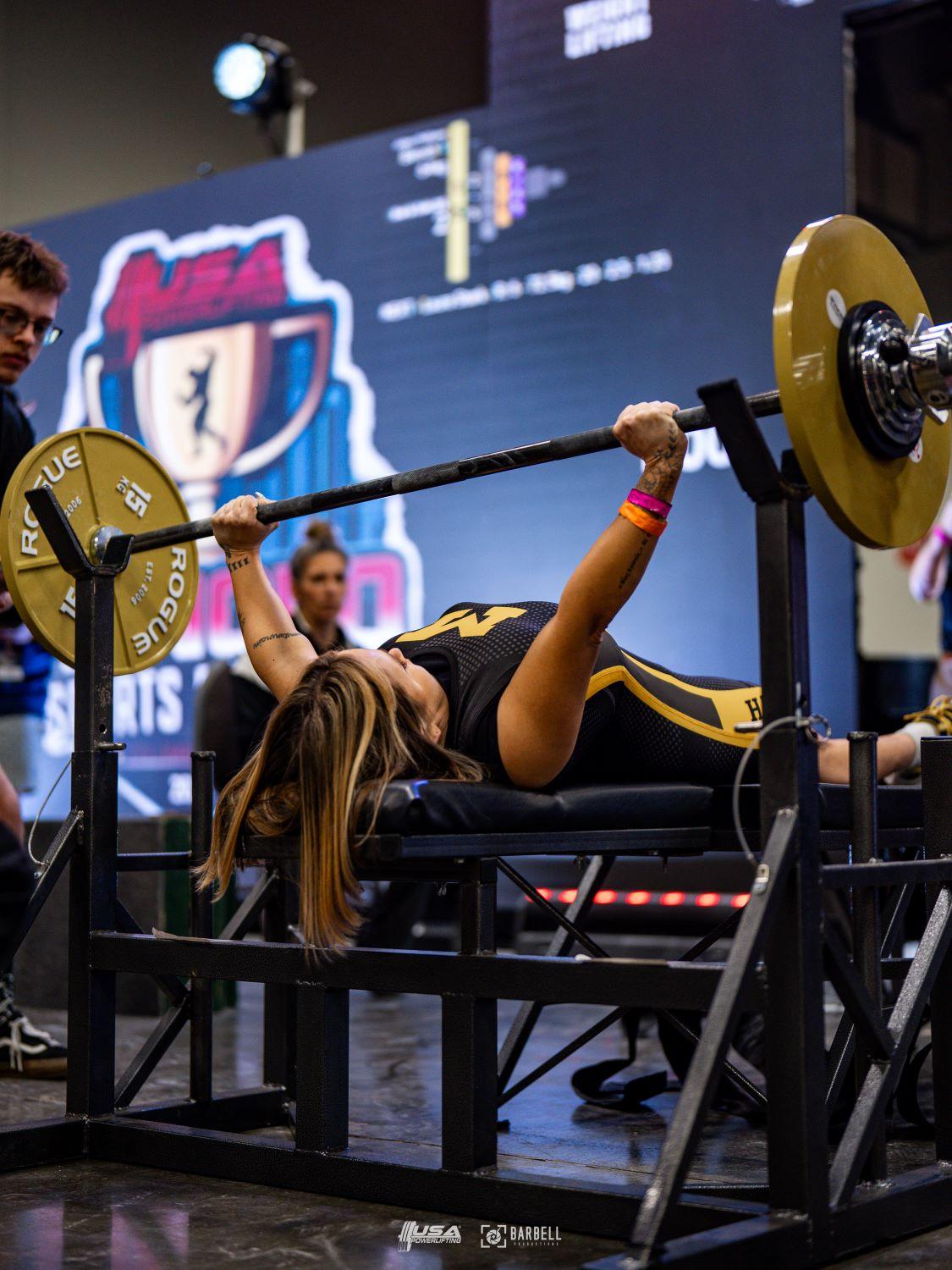 An athlete laying flat on a bench with the legs on the bench pressing the bar and plates with arms fully extended