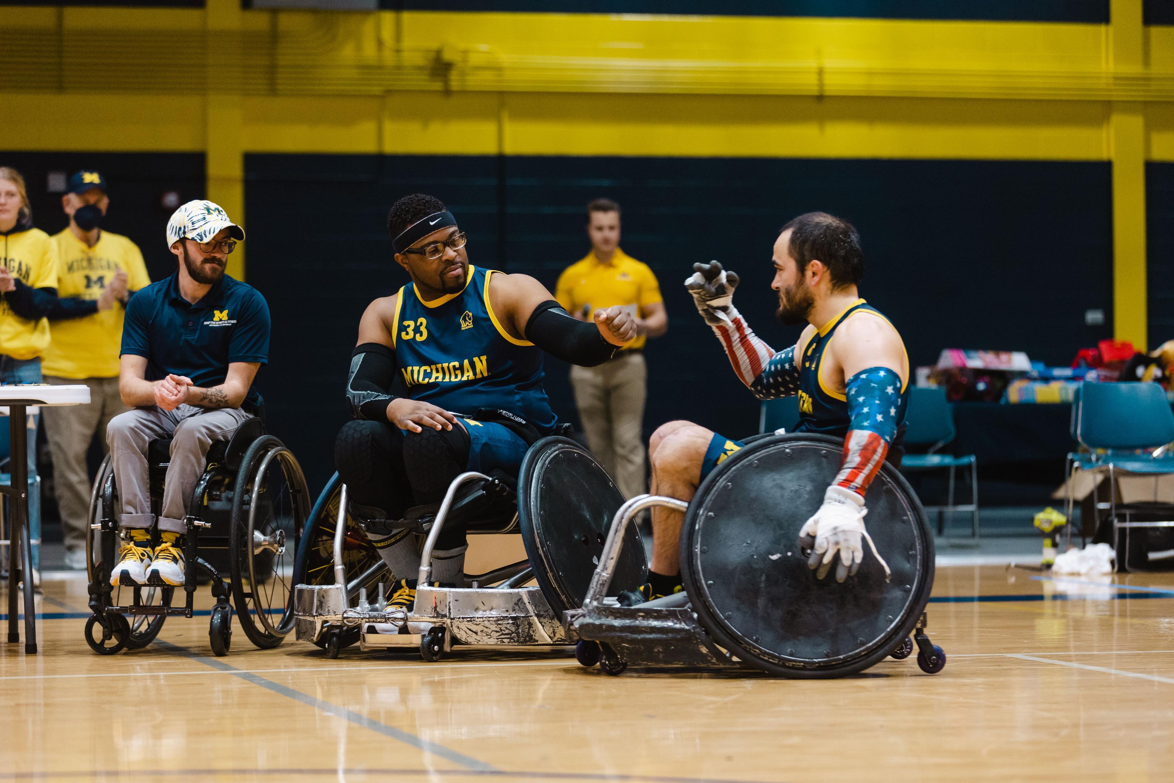 Two people in rugby wheelchairs fist bumping on the sidelines