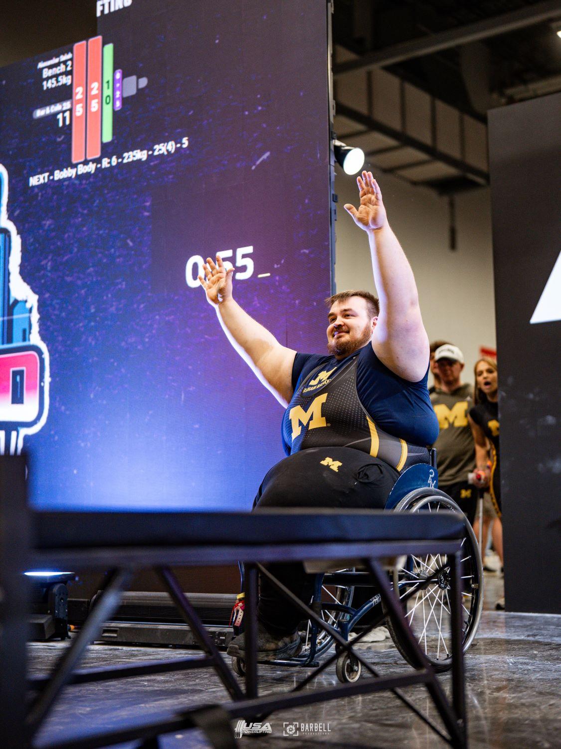 An athlete with both arms up wheeling onto the stage getting ready to lift