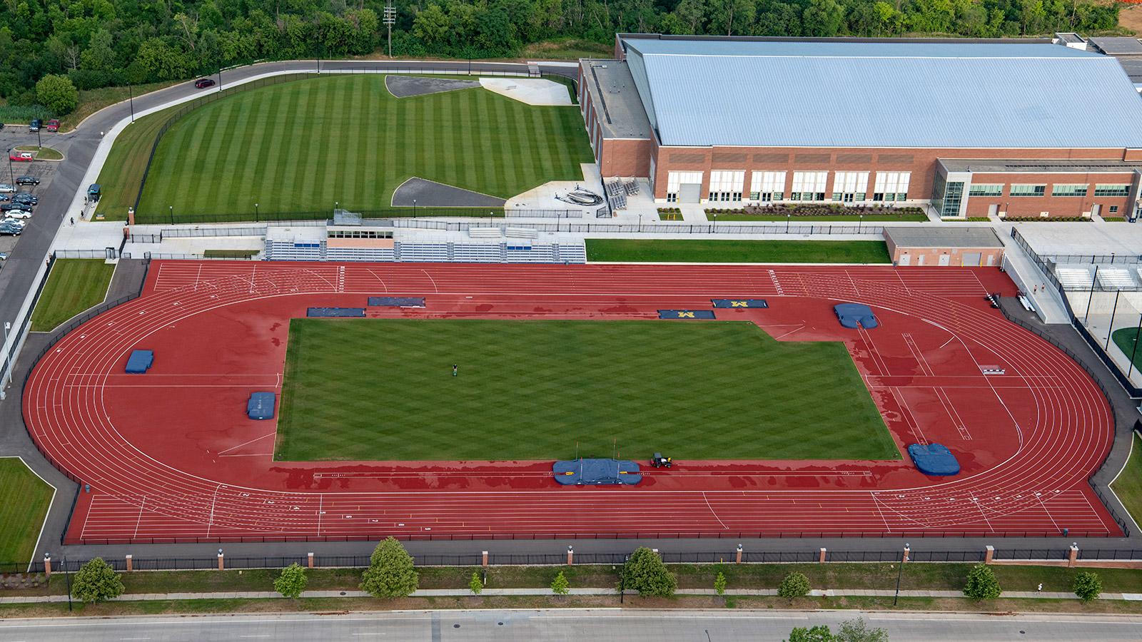 An aerial photograph of the University of Michigan outdoor varsity track with the field pits and indoor track building behind.