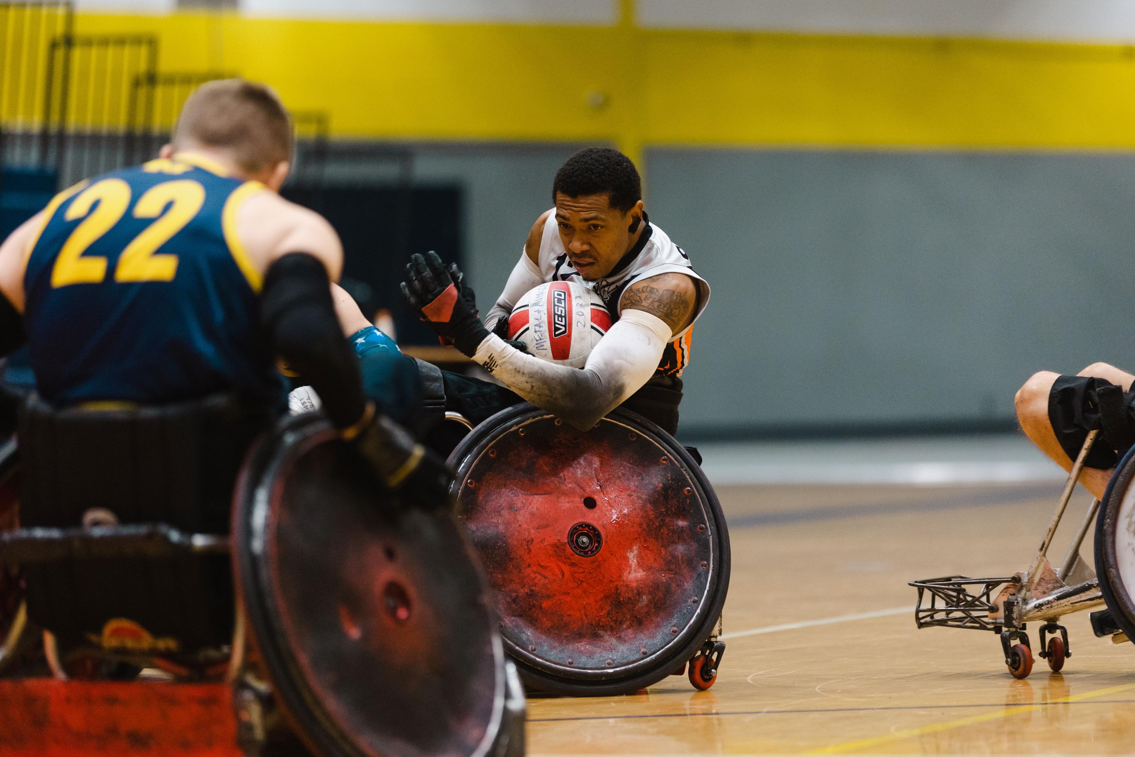A photo of an athlete protecting the ball as he pushes down the court while playing wheelchair rugby