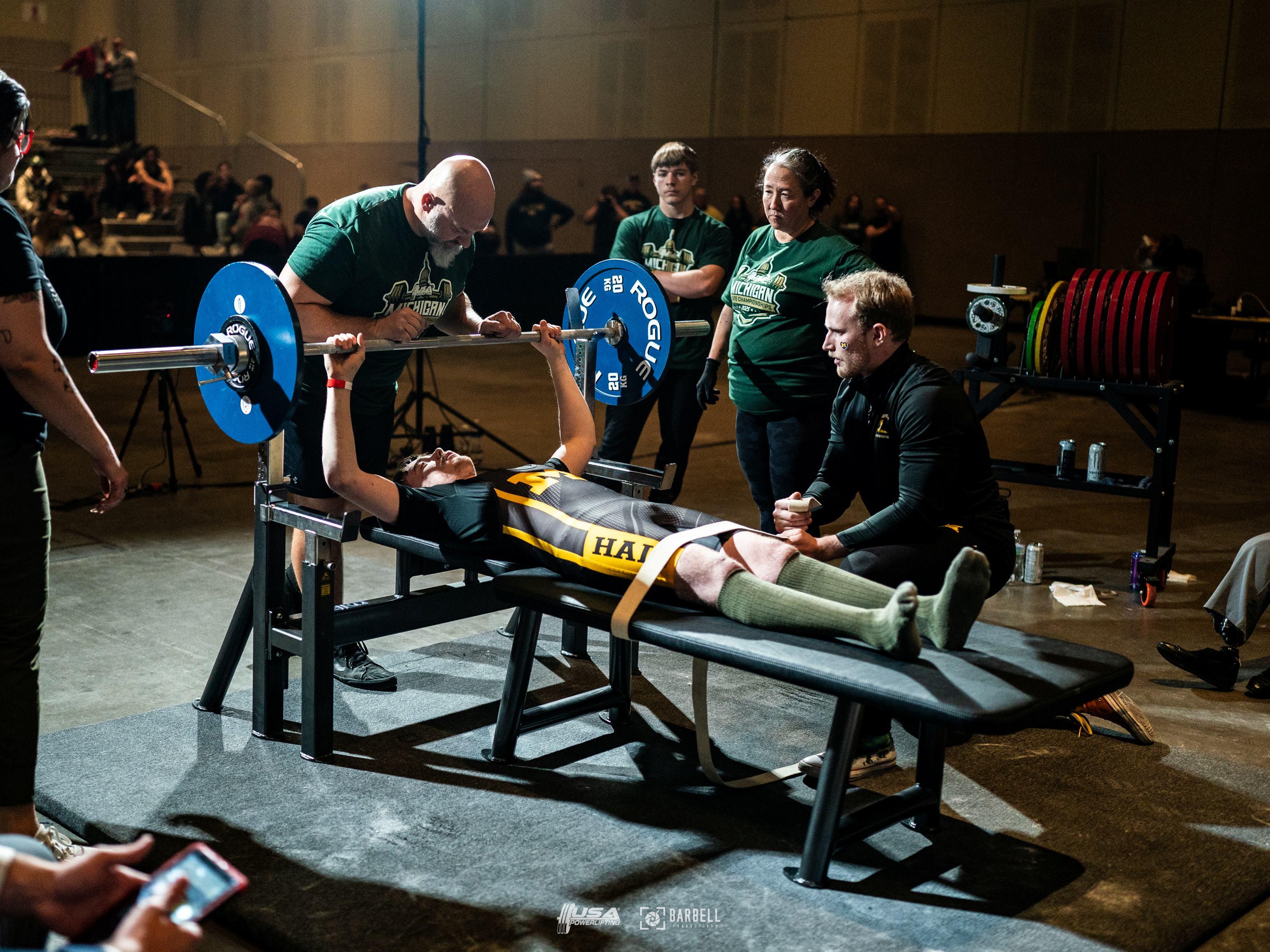An athlete laying flat on a bench lifting a bar with plates on each side