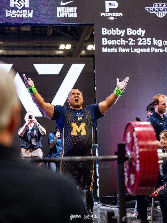 A single leg amputee walking up to a bench with a loaded bar getting ready to lift