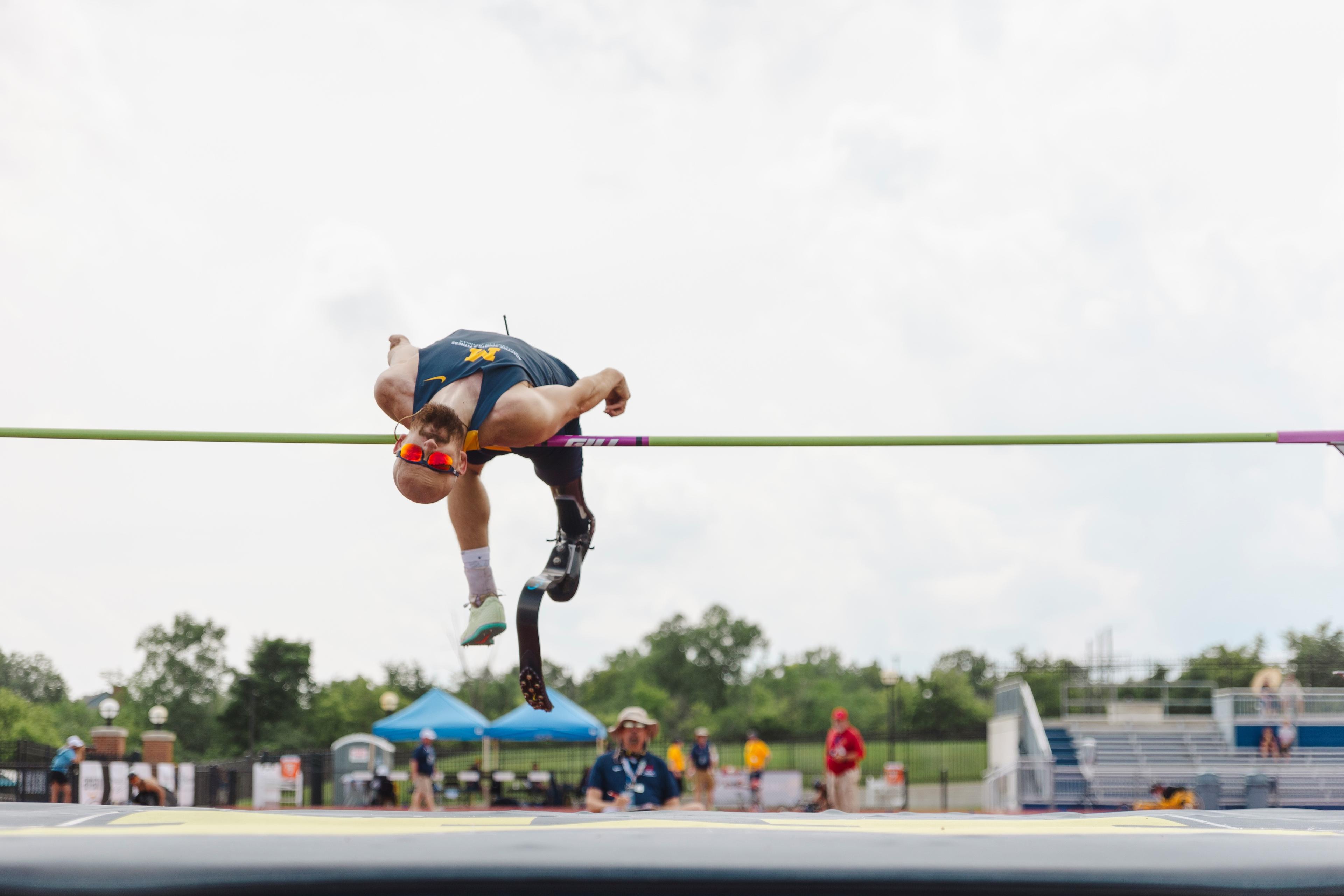 Adaptive athlete with a prosthetic leg mid-air and arched over the bar competing in the high jump competition